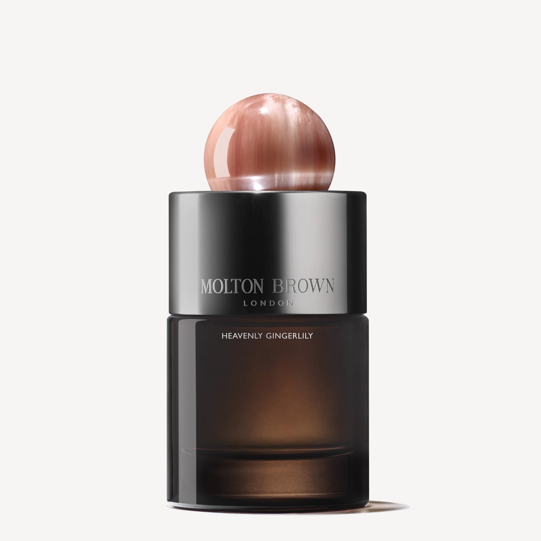 A sleek, dark hervulbare glazen flacon of MoltonBrown Nederlands Heavenly Gingerlily Eau de Parfum 100ml, with a metallic cap and round pink marble-like topper, is set against a plain white background.