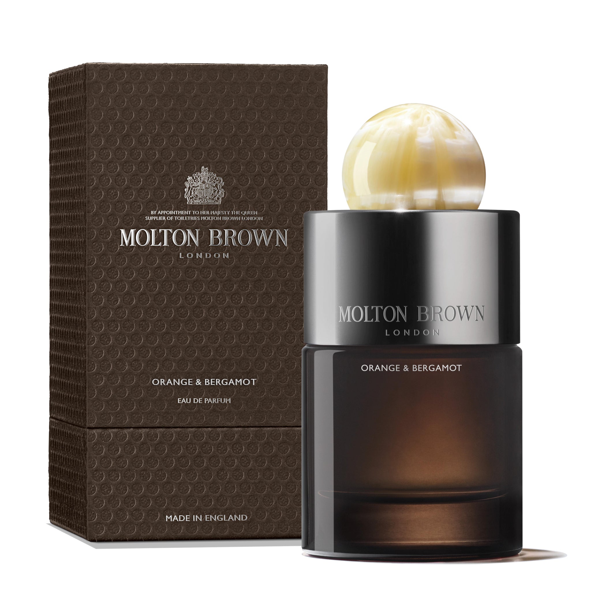 A 100ml Orange & Bergamot Eau de Parfum bottle by MoltonBrown Nederlands, topped with a round marbled cap, sits next to its textured brown box; both display silver and white text and hint at subtle patchouli notes.