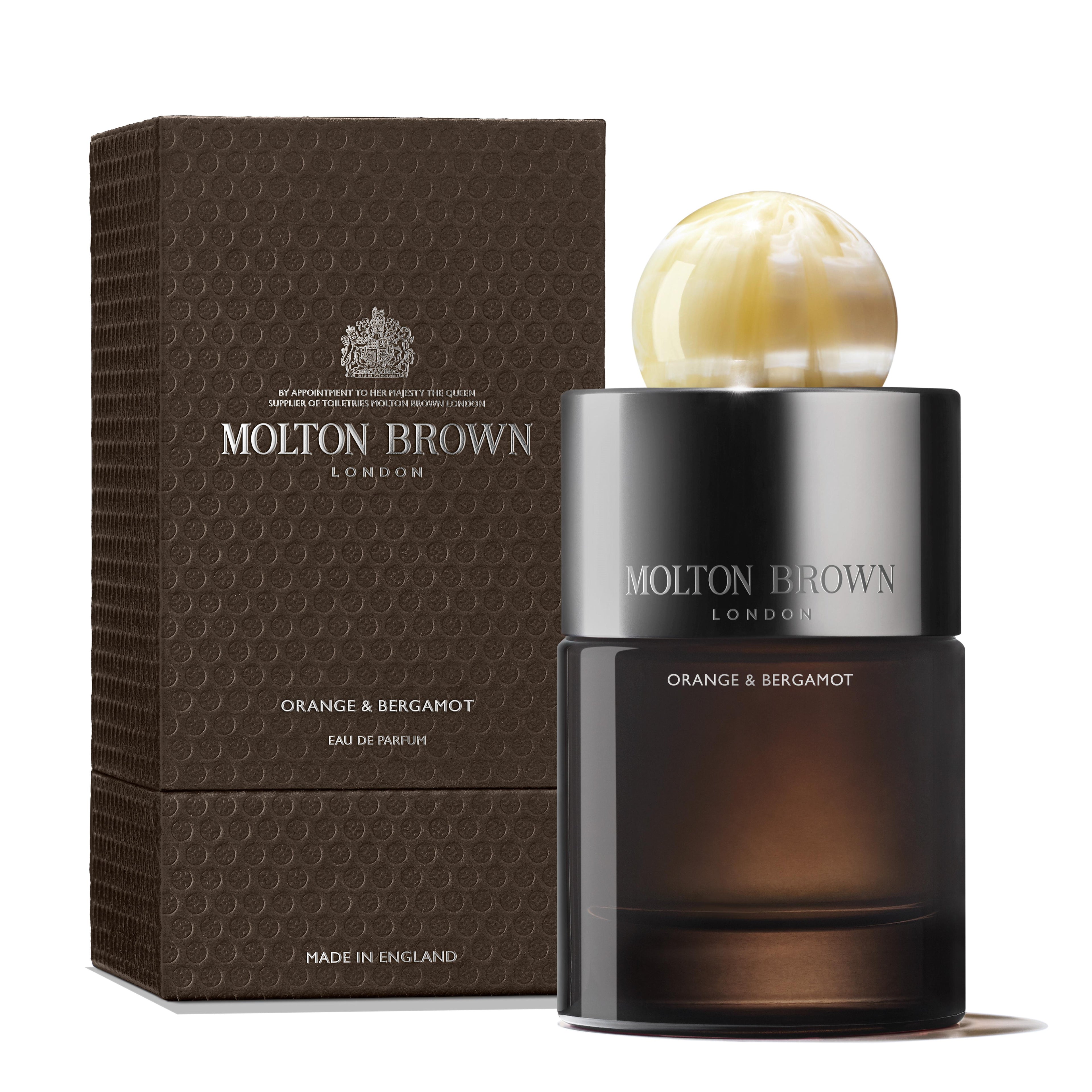 A 100ml Orange & Bergamot Eau de Parfum bottle by MoltonBrown Nederlands, topped with a round marbled cap, sits next to its textured brown box; both display silver and white text and hint at subtle patchouli notes.