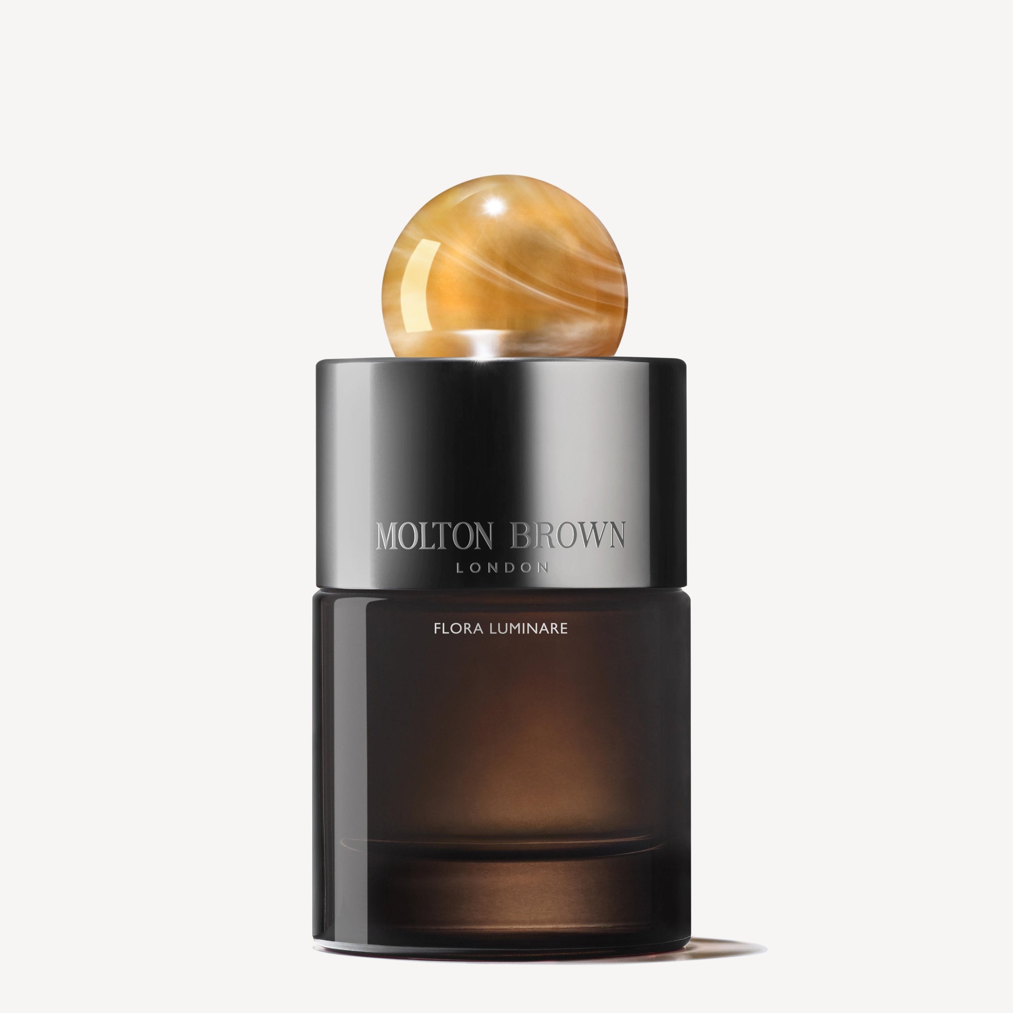 A dark cylindrical MoltonBrown Nederlands Flora Luminare Eau de Parfum 100ml bottle with a glossy marbled gold sphere cap, set against a plain white background.