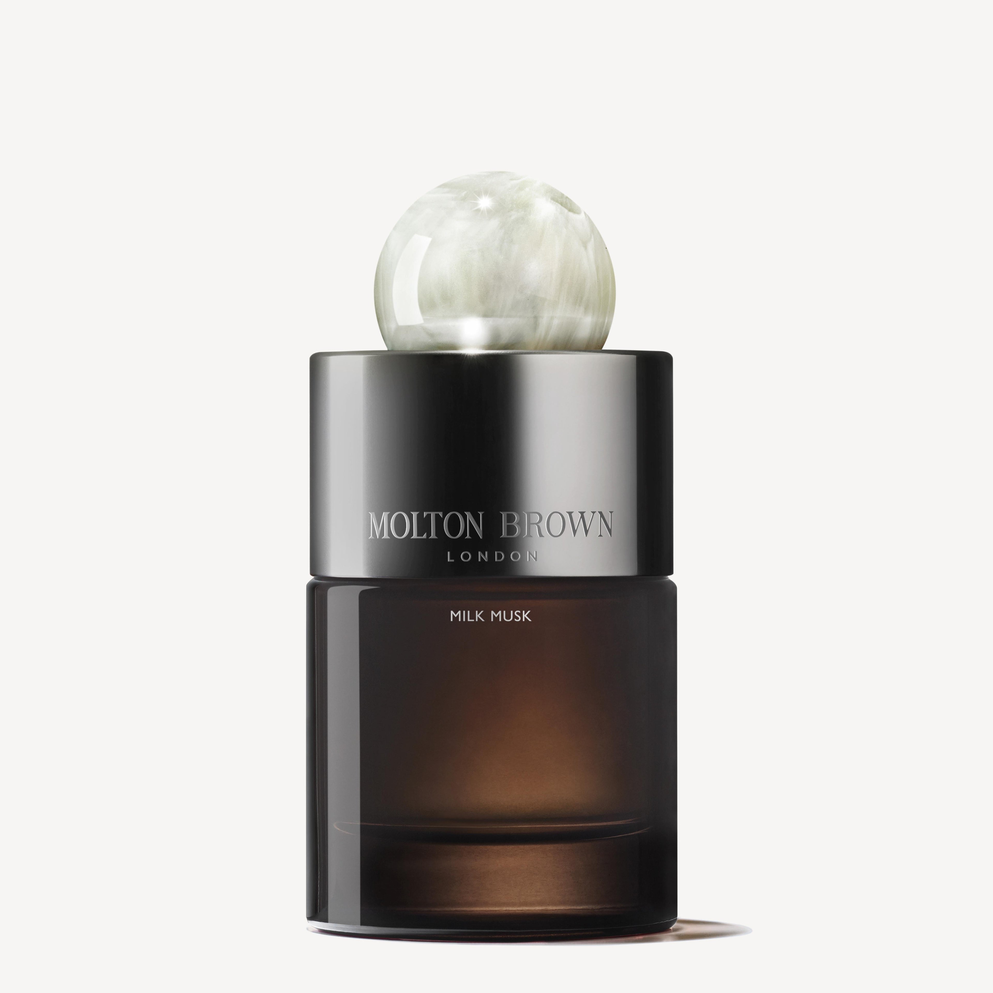 A 100ml MoltonBrown Nederlands Milk Musk Eau de Parfum bottle with a marble-look spherical cap and dark, semi-transparent body is set against a white background, evoking pear and musk notes.
