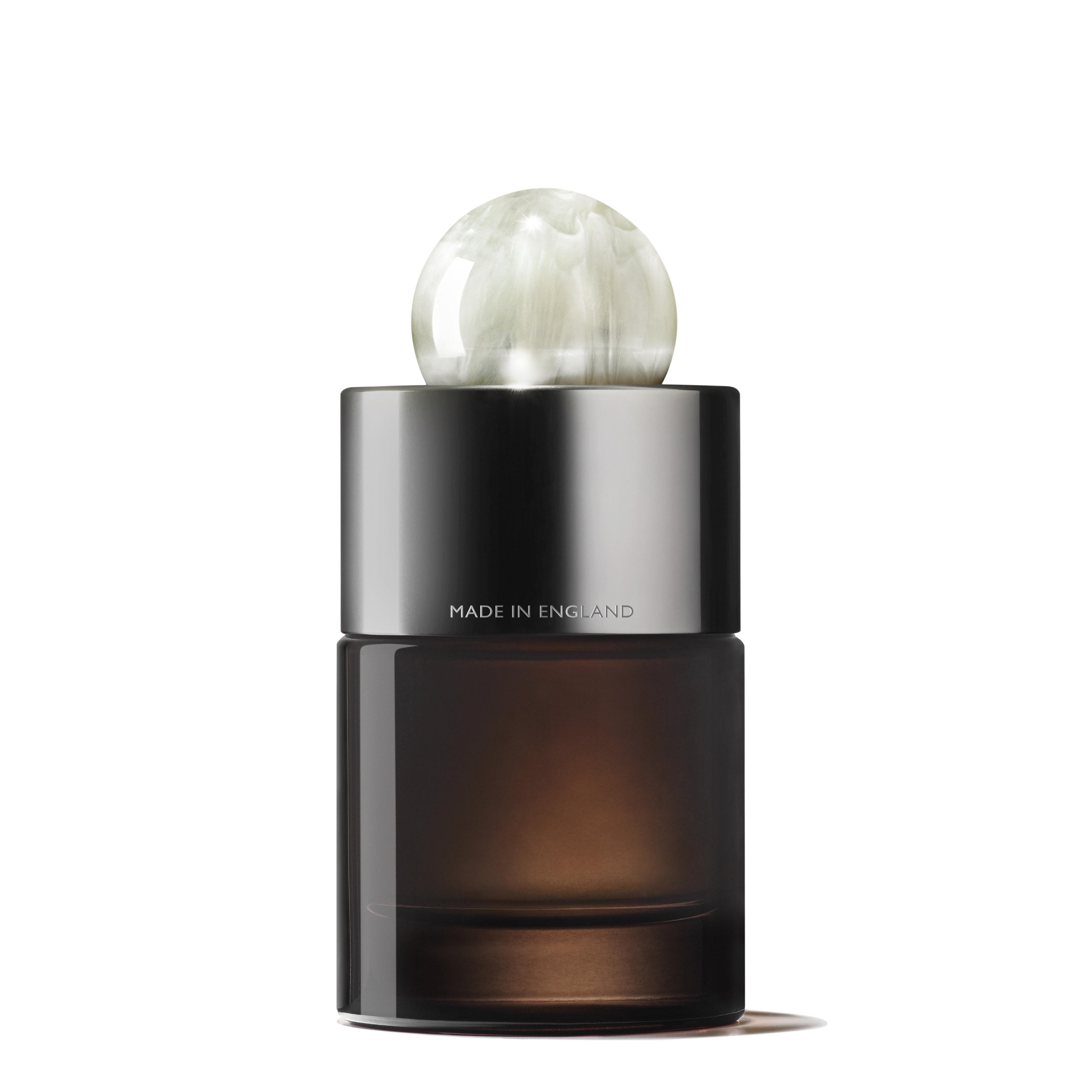 The MoltonBrown Nederlands Milk Musk Eau de Parfum 100ml comes in a dark glass bottle with a metallic silver collar and round marbled white cap, engraved "MADE IN ENGLAND." The plain white background highlights its subtle vanille notes.