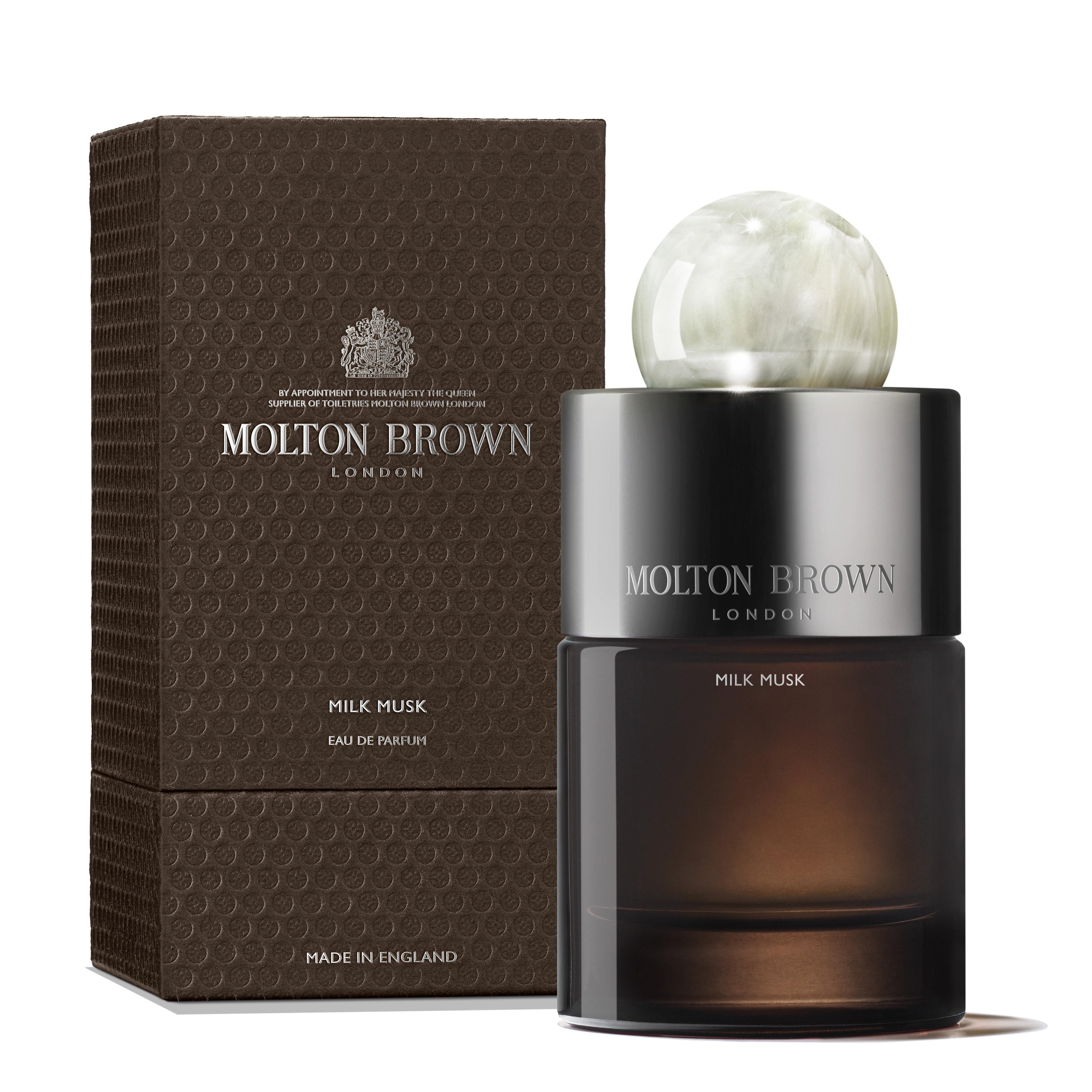 A 100ml bottle of MoltonBrown Nederlands Milk Musk Eau de Parfum, with notes of vanille, peer en musk, stands next to its textured dark brown box. A marble-style cap and label highlight its Engelse afkomst.