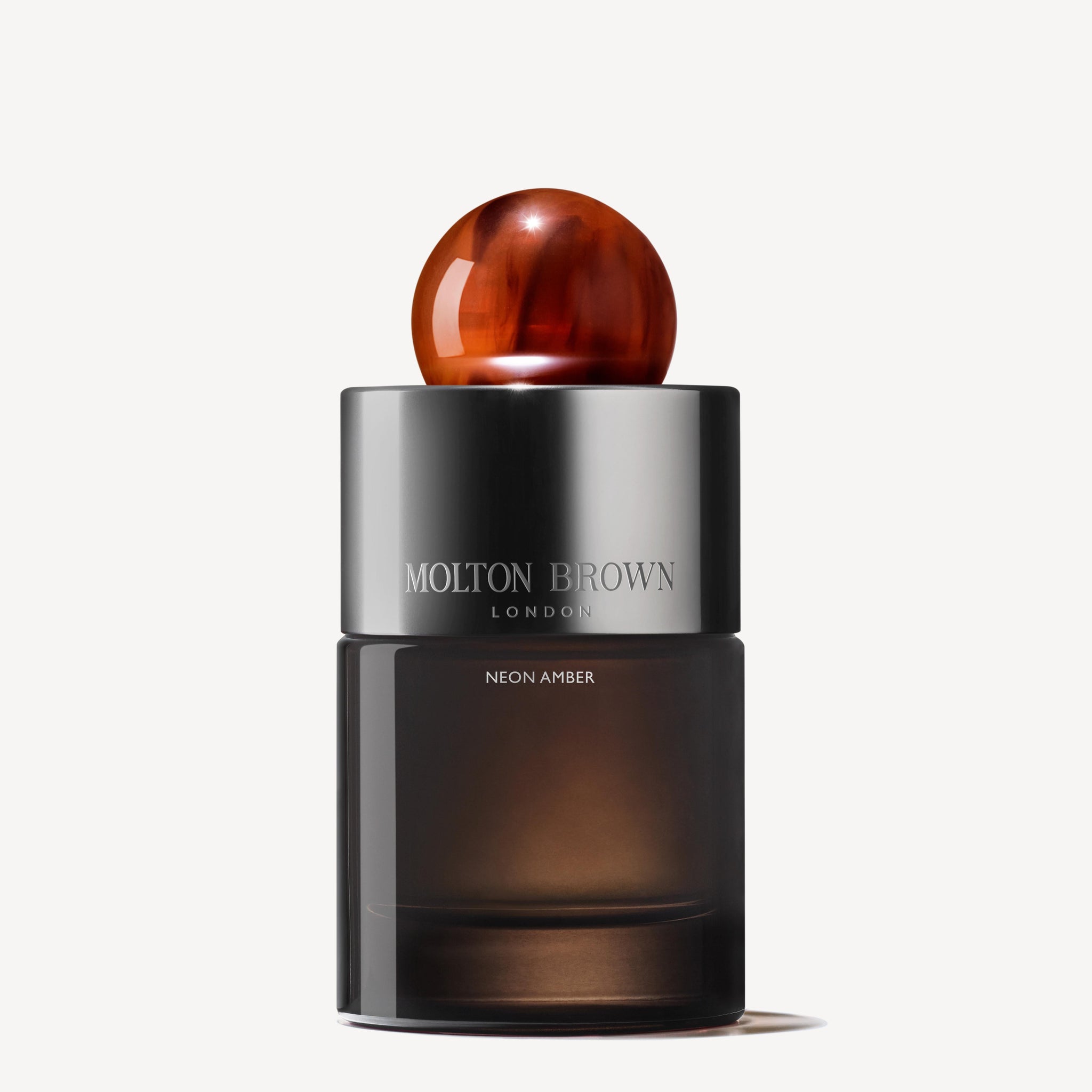 A 100ml bottle of MoltonBrown Nederlands Neon Amber Eau de Parfum, featuring a metallic silver label, translucent dark base, and round amber cap, displayed on a white background.
