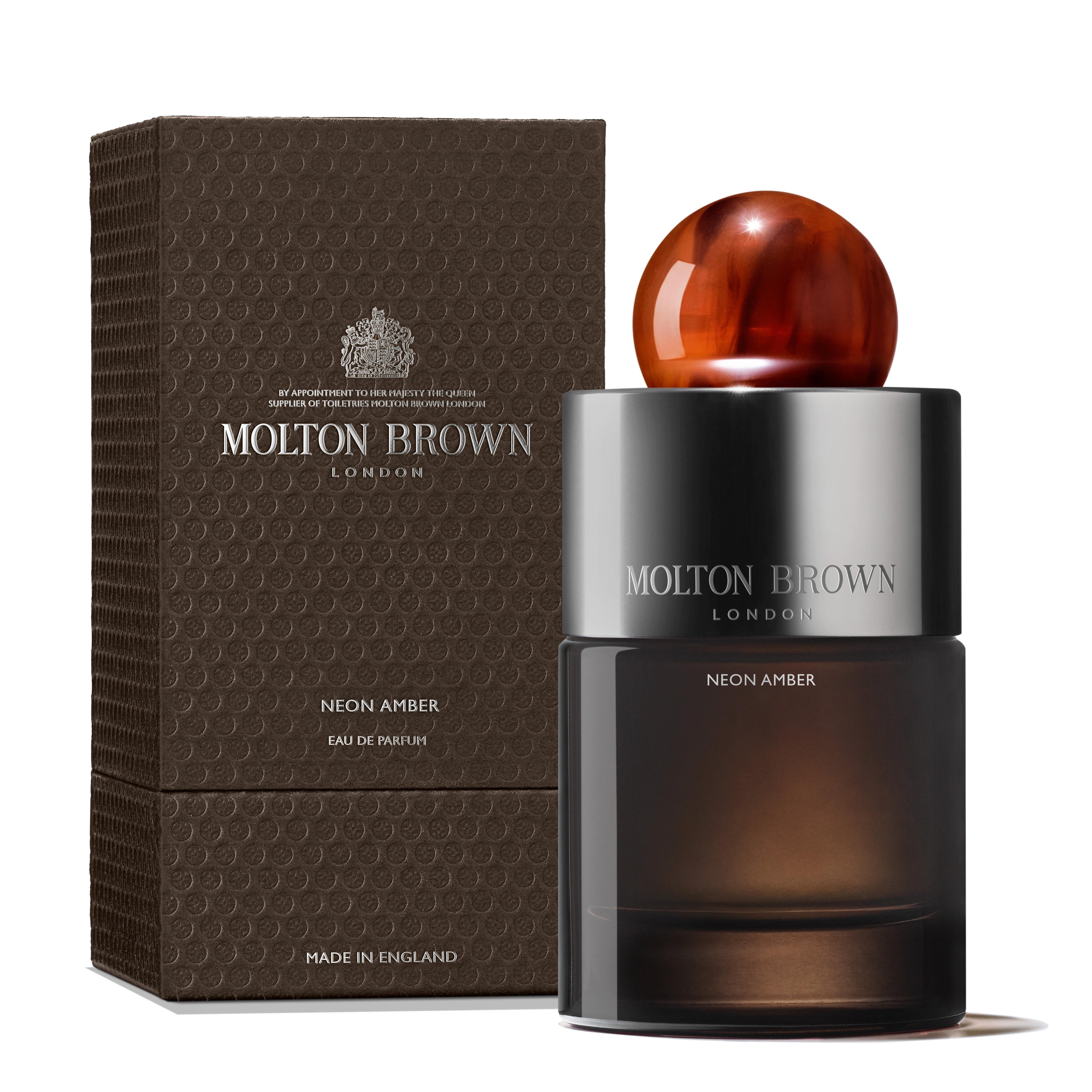A 100ml bottle of MoltonBrown Nederlands Neon Amber Eau de Parfum with a brown spherical cap stands by its textured brown box, which features silver and white text and highlights notes of tonkaboon and cederhout.
