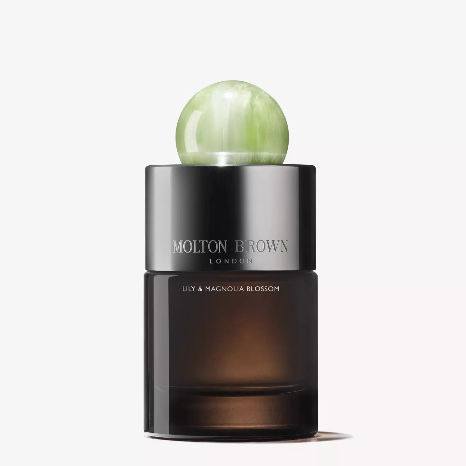 A dark glass MoltonBrown Nederlands Lily & Magnolia Blossom Eau de Parfum 100ml bottle with a metallic cap and pale green marble-like round top, set against a plain white background.