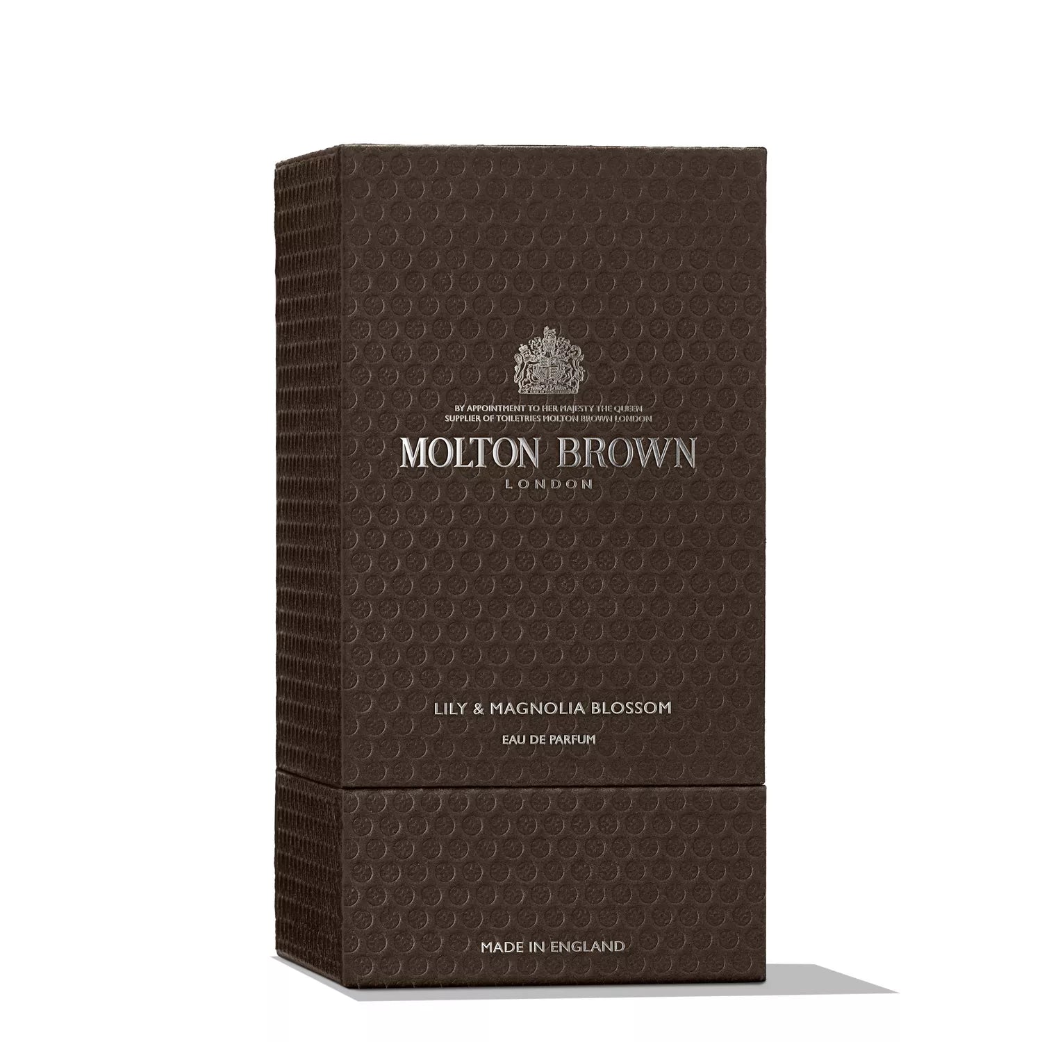 A dark brown textured box of MoltonBrown Nederlands Lily & Magnolia Blossom Eau de Parfum 100ml, detailed with silver branding and product info, stands upright against a white background—a sophisticated tribute to vetiver notes.