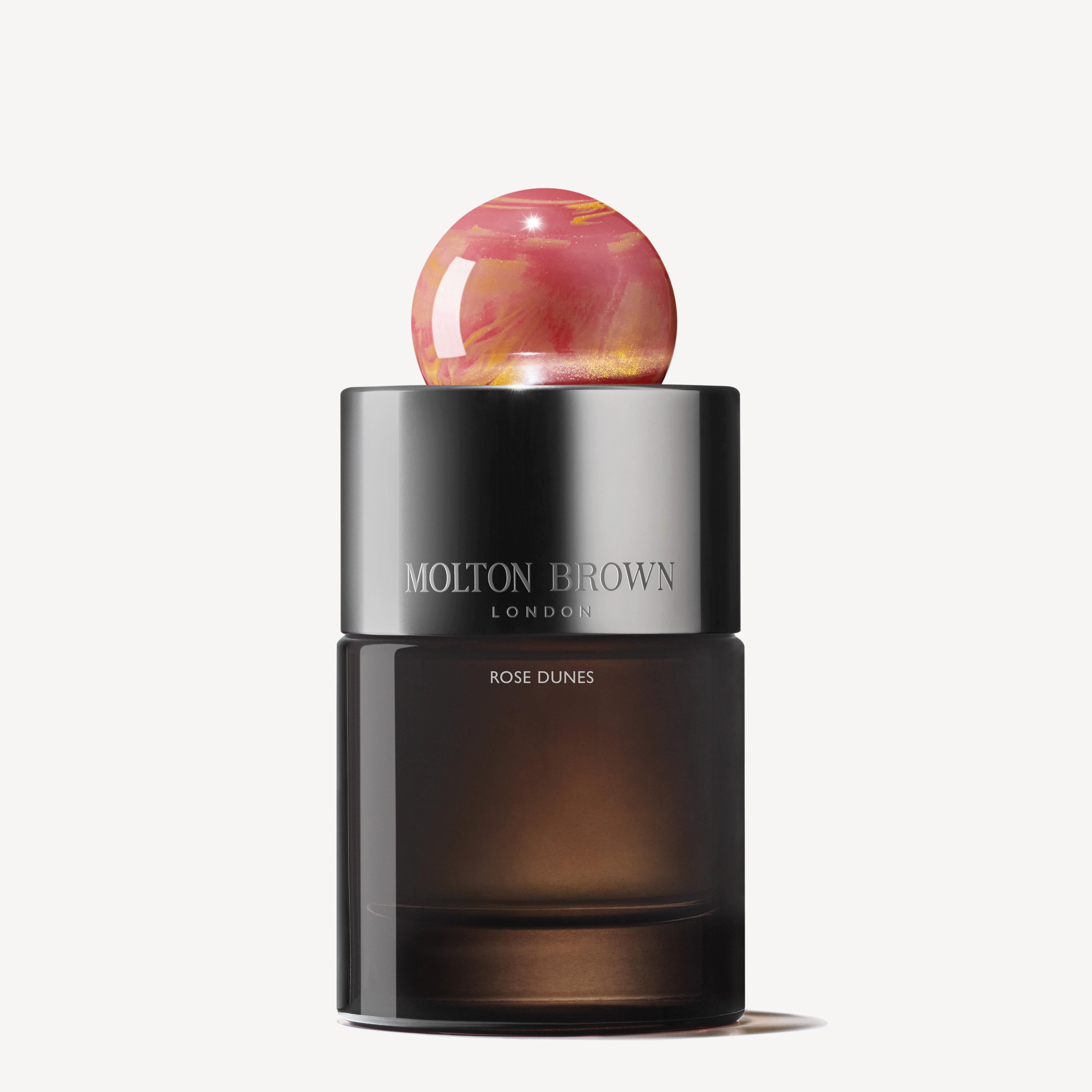 A 100ml MoltonBrown Nederlands Rose Dunes Eau de Parfum bottle, featuring a dark translucent base, sleek black cap, and round pink marbled stopper, set against a plain white background.