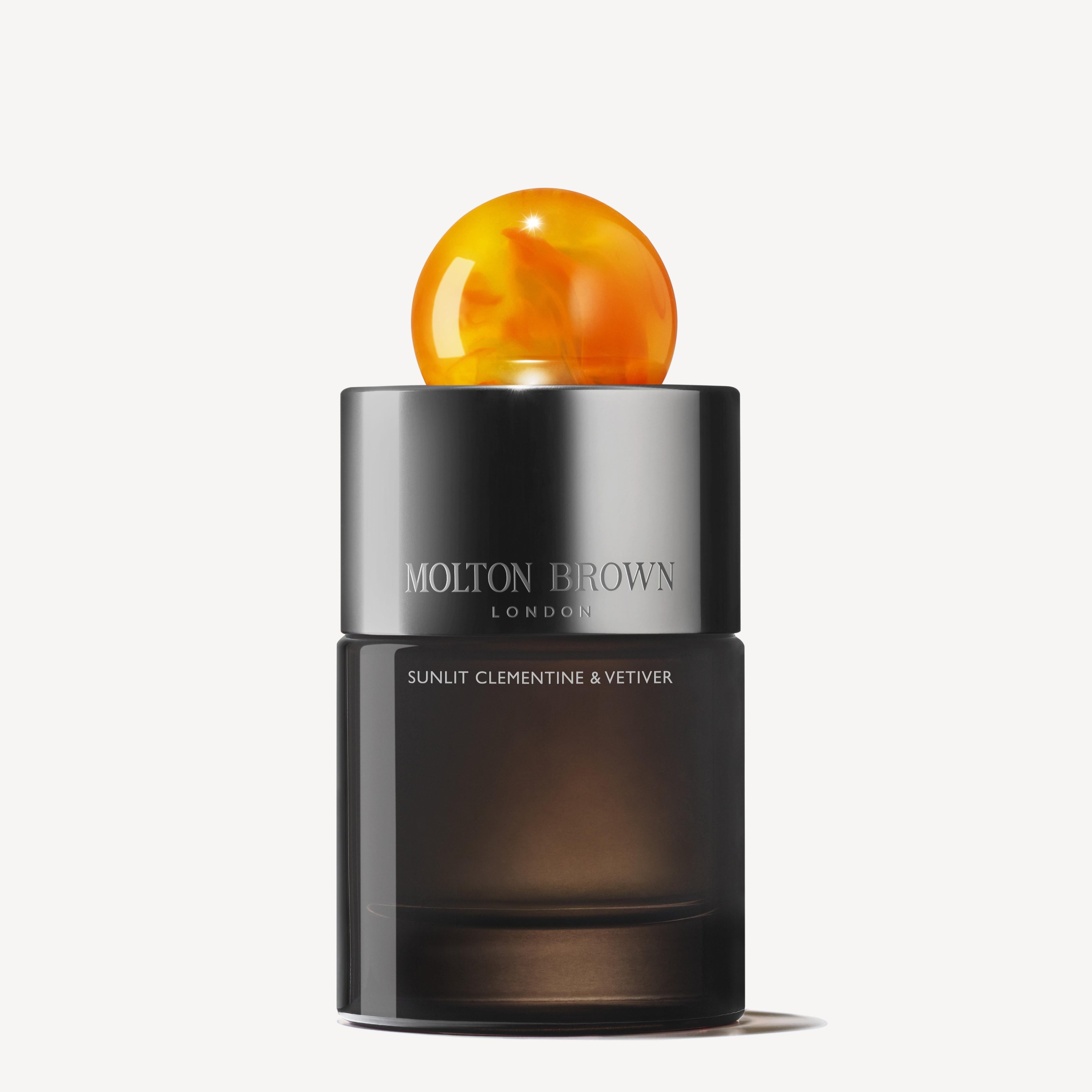 A black cylindrical MoltonBrown Nederlands Sunlit Clementine & Vetiver Eau de Parfum 100ml bottle, with a round marbled orange cap and silver branded band, stands against a white background voor een stijlvolle en langdurige indruk.