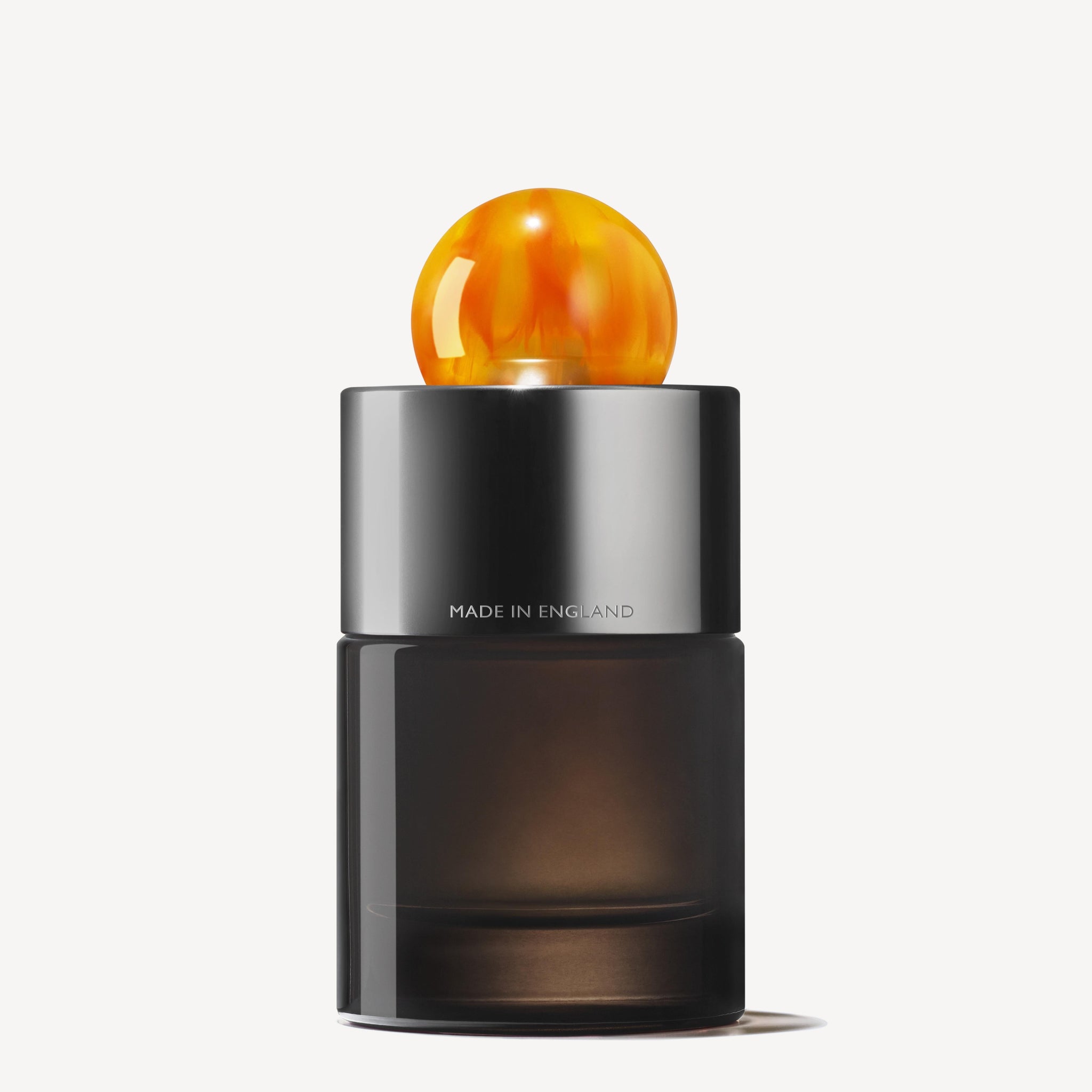 A sleek, dark glass bottle of MoltonBrown Nederlands Sunlit Clementine & Vetiver Eau de Parfum 100ml features a shiny silver cap with a round amber topper. "MADE IN ENGLAND" is visible, set against a plain white background.