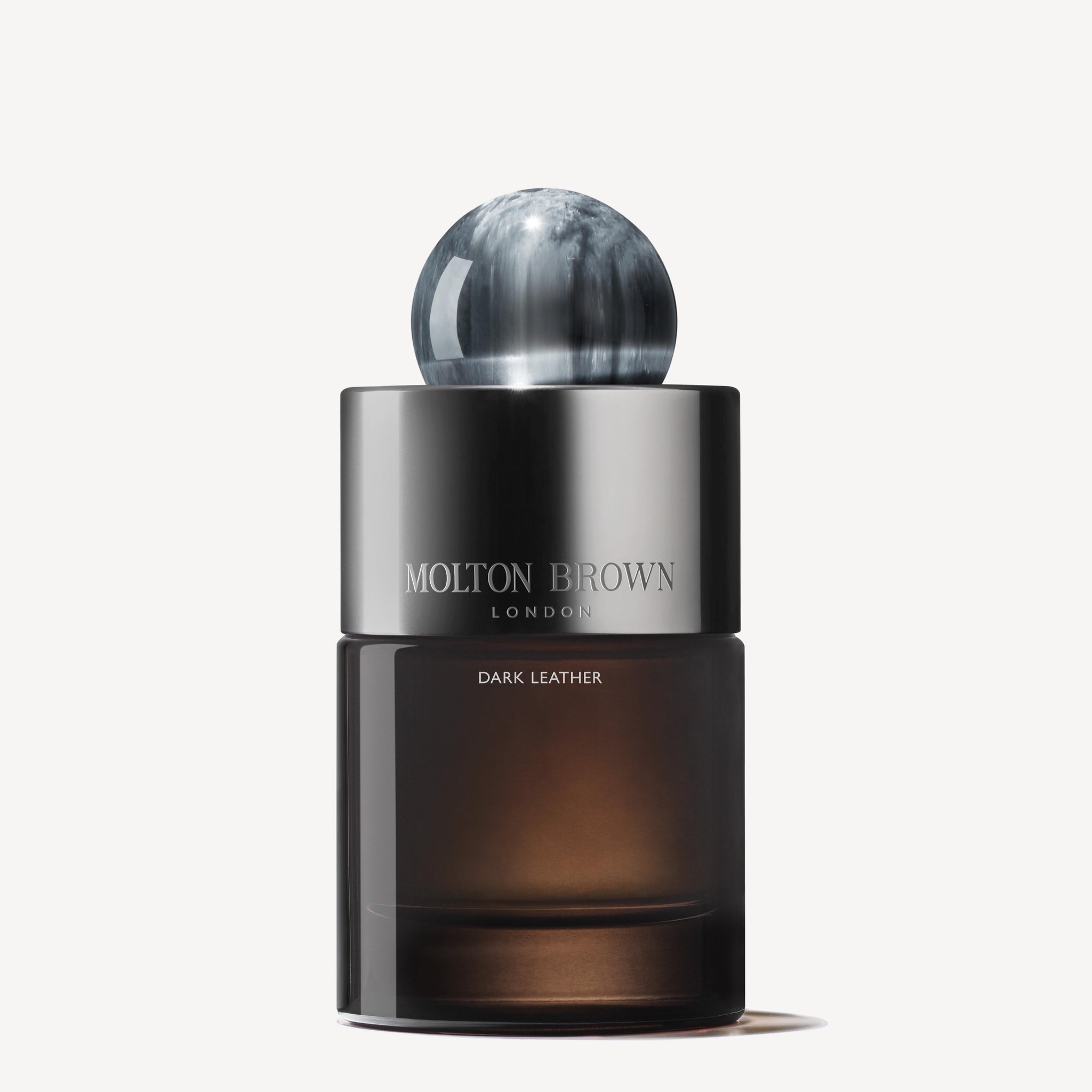 A 100ml bottle of MoltonBrown Nederlands Dark Leather Eau de Parfum, featuring a smoky base, silver band, and marbled black-and-white cap, is set against a white background. Subtle musky notes linger in the air.