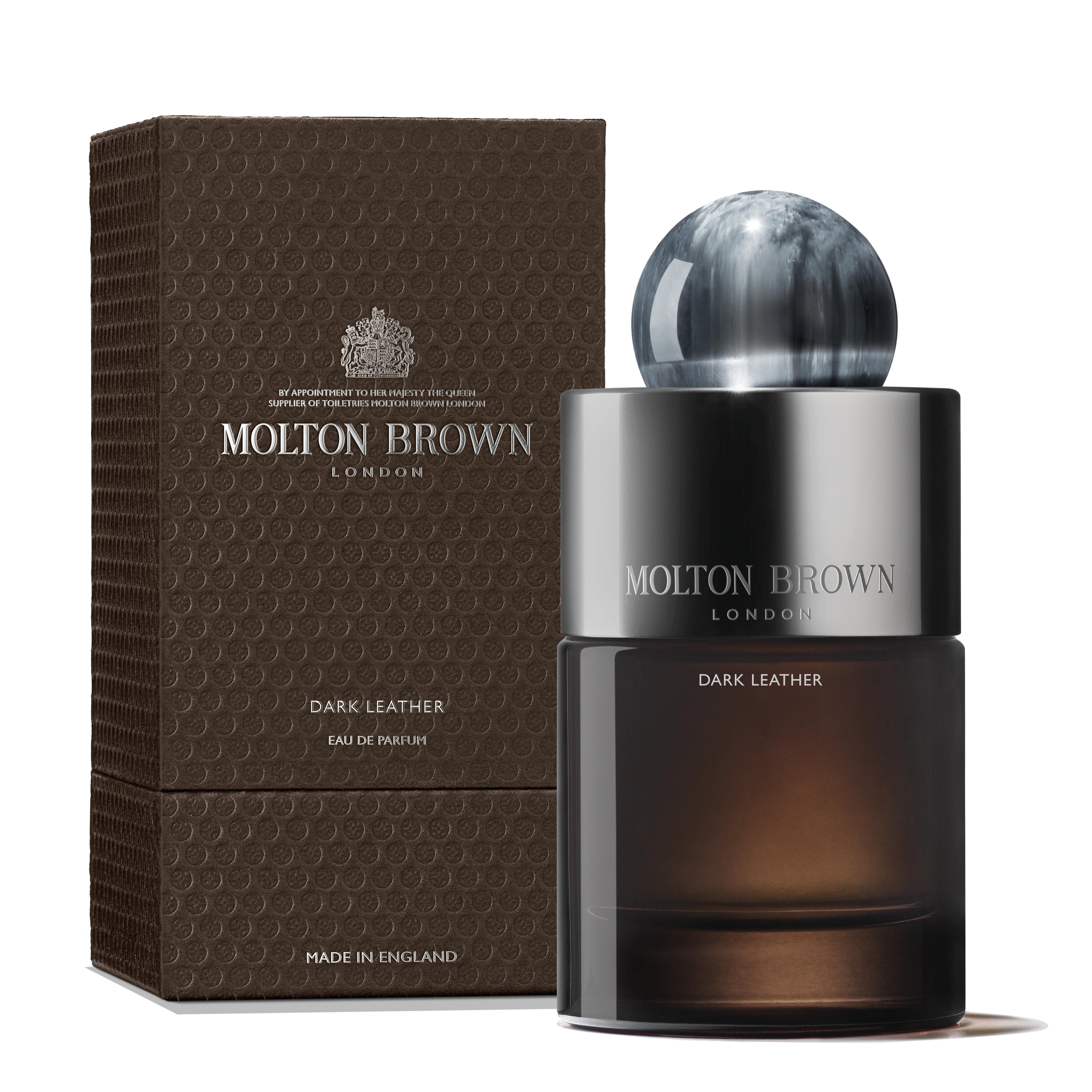 A bottle of MoltonBrown Nederlands Dark Leather Eau de Parfum 100ml with a round marbled cap sits beside its textured dark brown box, both featuring the brand's logo and elegant silver lettering, evoking a musky essence.
