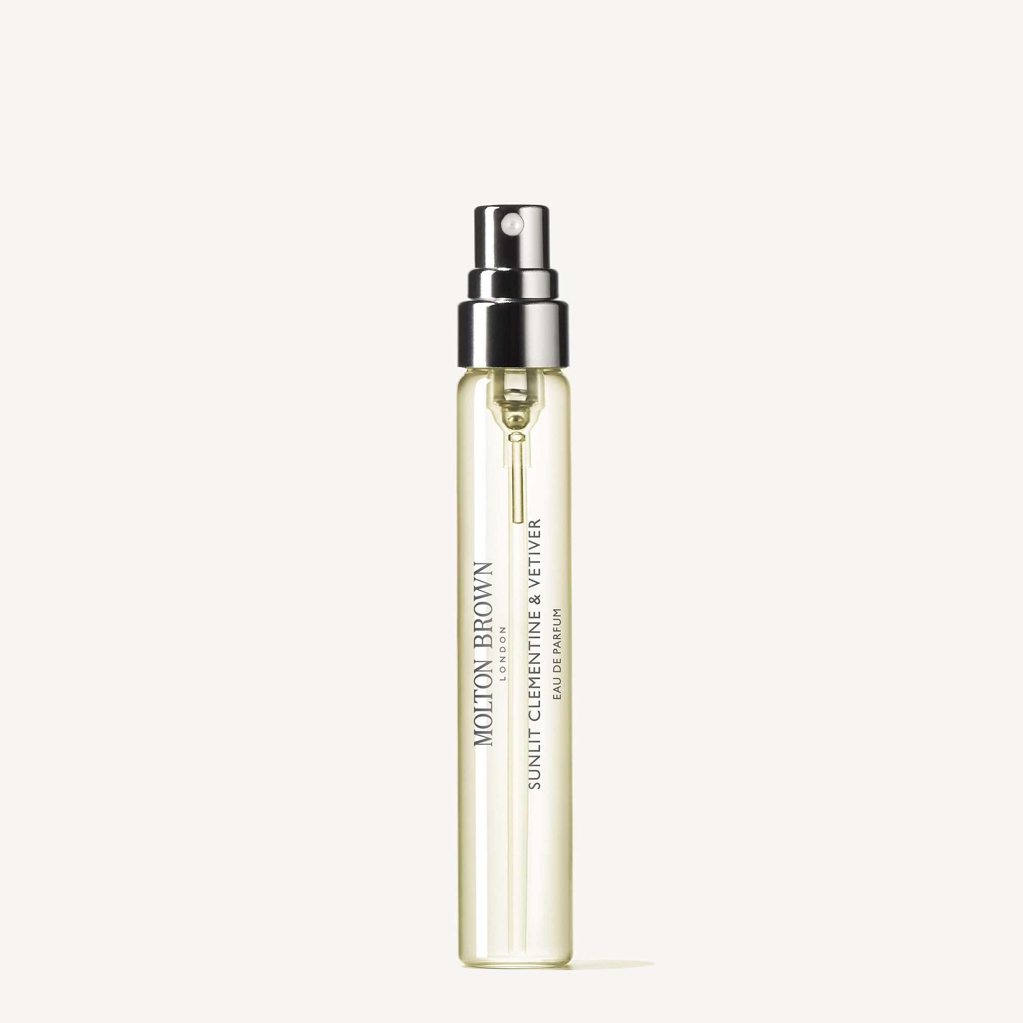 A clear glass travel spray bottle (7.5ml) with a black and silver nozzle contains yellow Sunlit Clementine & Vetiver Eau de Parfum by MoltonBrown Nederlands. The simple white background highlights this luxe reiskoffer navulling.