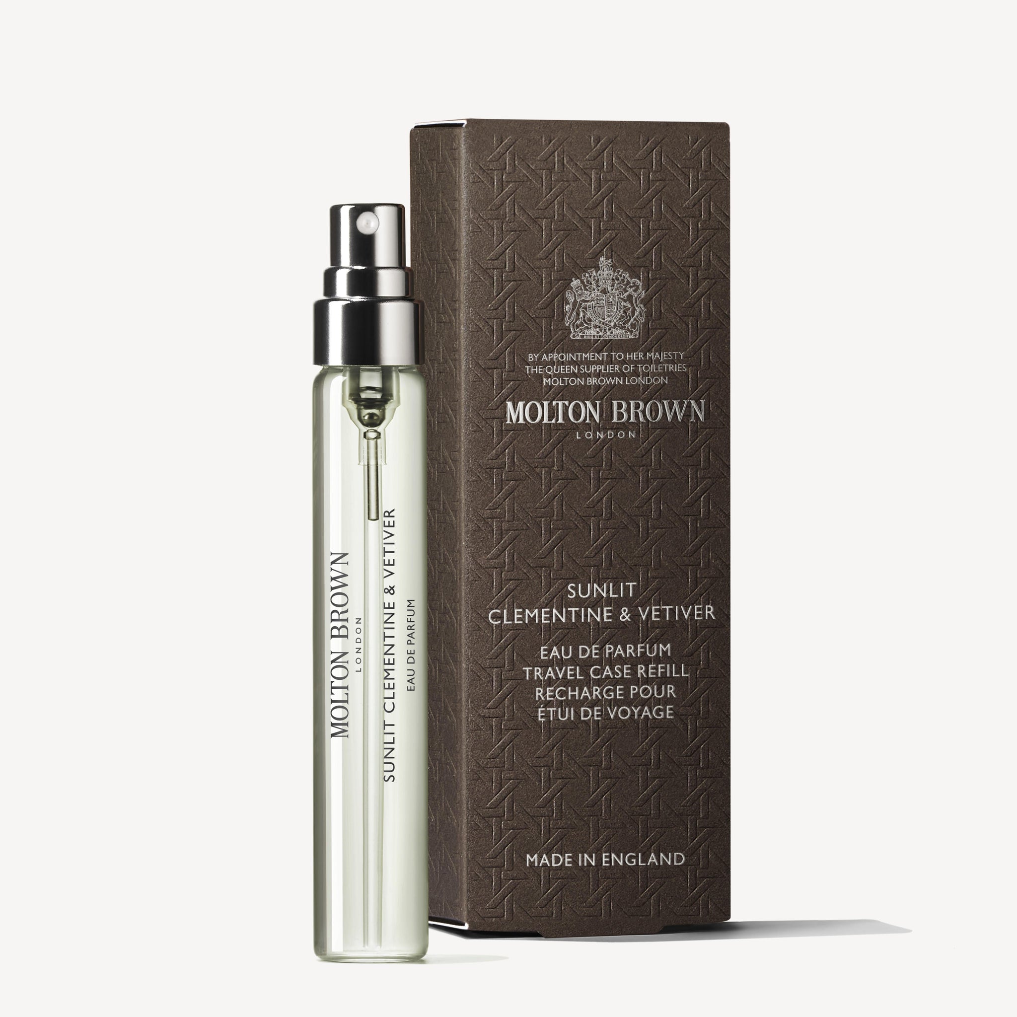 A clear glass MoltonBrown Nederlands Sunlit Clementine & Vetiver Eau de Parfum Reiskoffer Navulling 7.5ml sits beside a matching brown, textured box with silver text, both displayed against a white background.