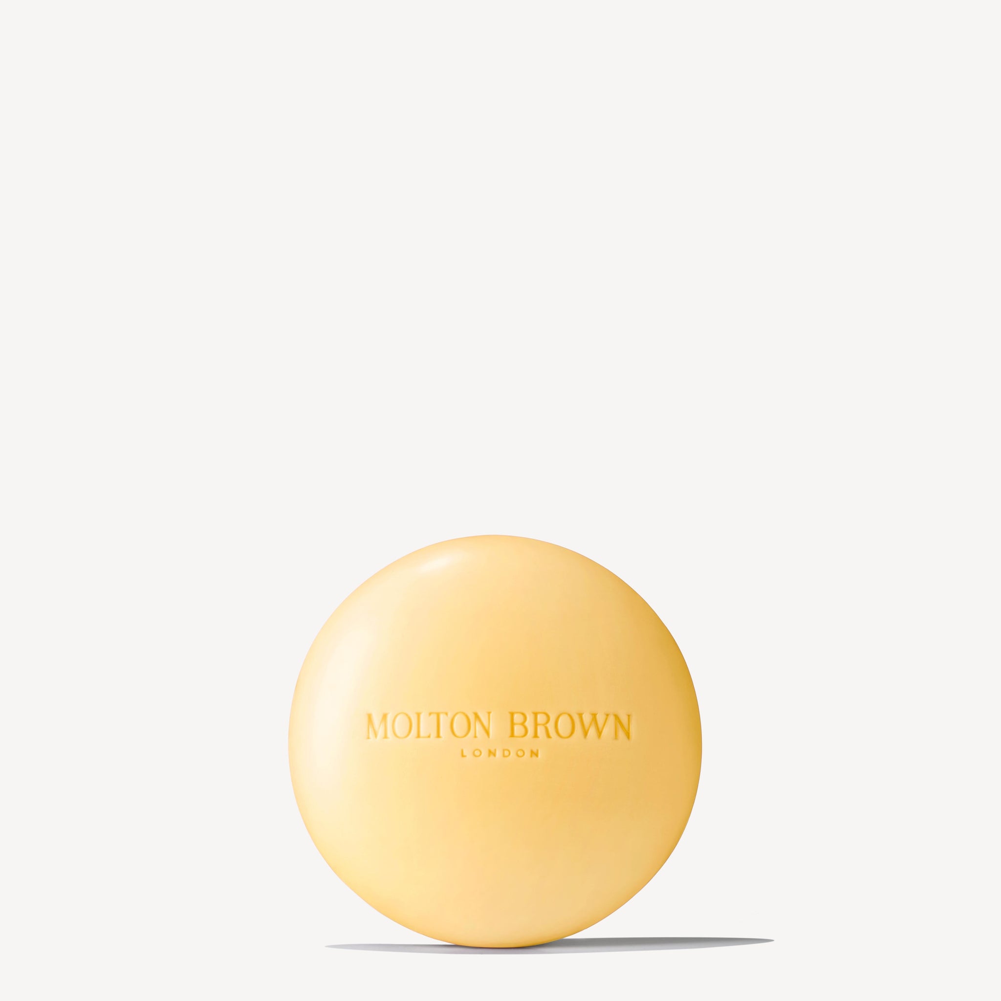 A round, yellow Orange & Bergamot Perfumed Soap 150g by MoltonBrown Nederlands, enriched with natuurlijke oliën and embossed with the brand name on the front, shown against a plain white background.