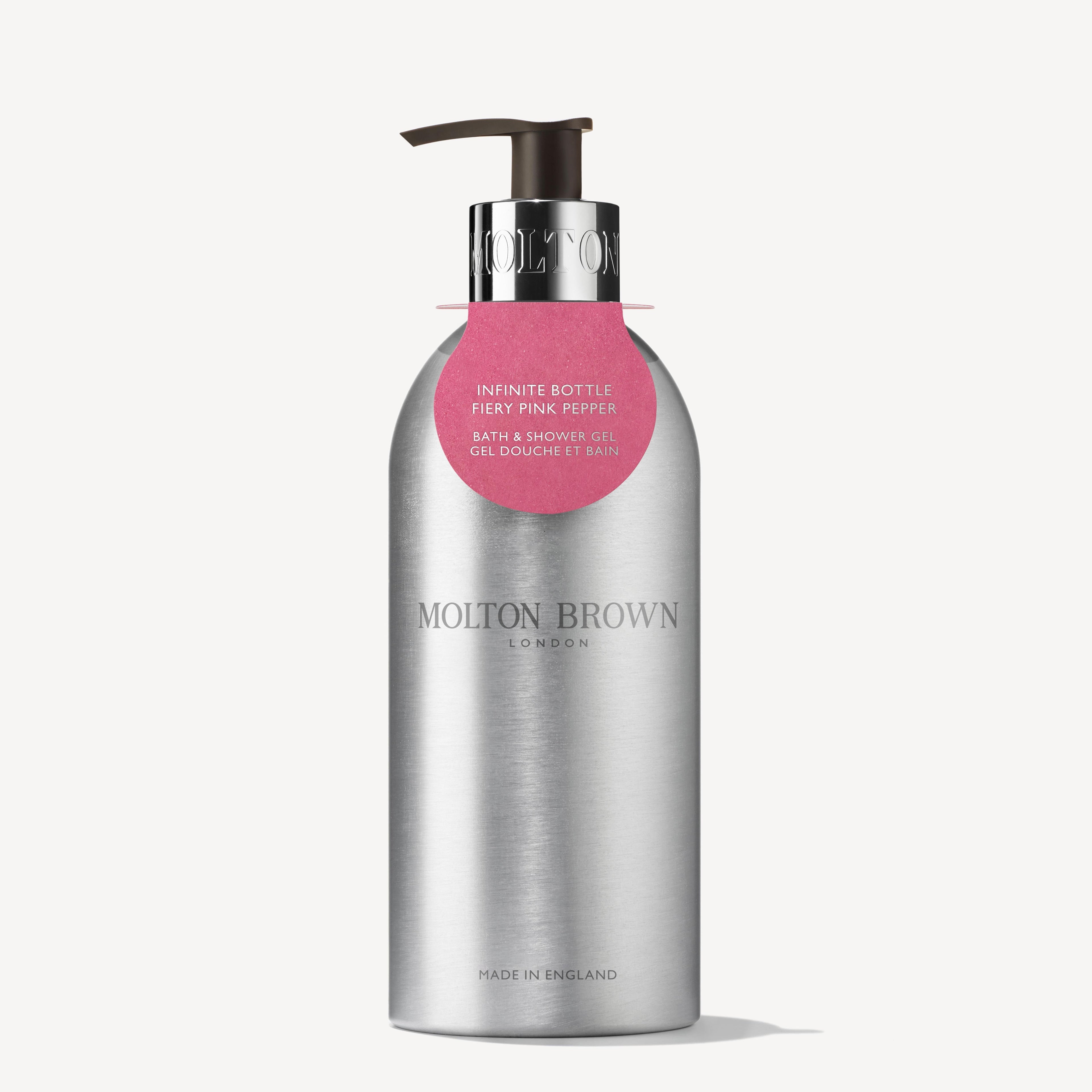A zilveren, gerecycleerde aluminium fles van MoltonBrown Nederlands met pomp, gelabeld "Fiery Pink Pepper Navulbare Fles 400ml". Zwarte tekst en logo vallen op, terwijl een roze label de houtig-kruidige douchegel accentueert.