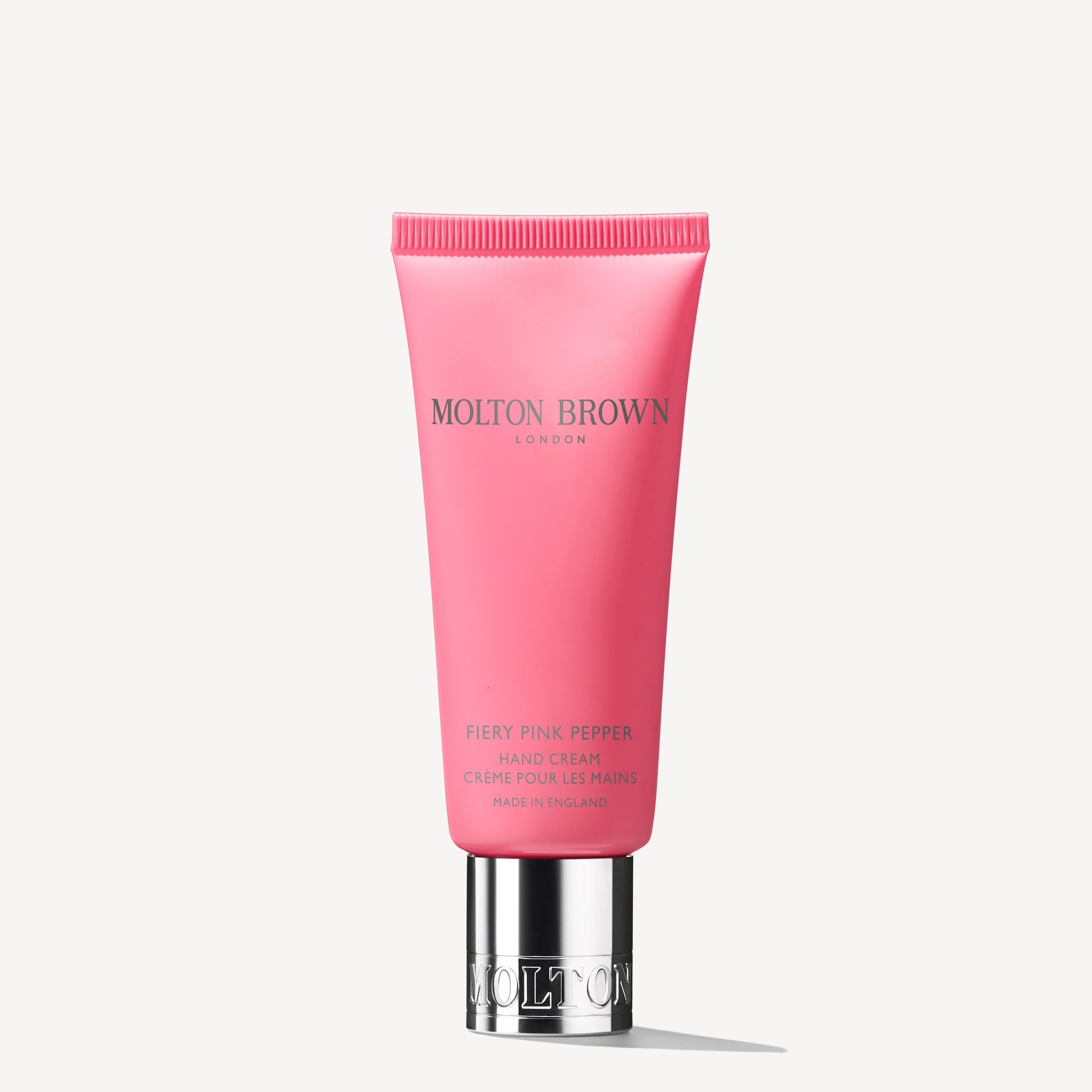 A pink tube of MoltonBrown Nederlands Fiery Pink Pepper Handcrème 40ml with a silver cap, upright on a white background. The text is printed in silver and gold, and the handcrème is enriched with sheaboter.