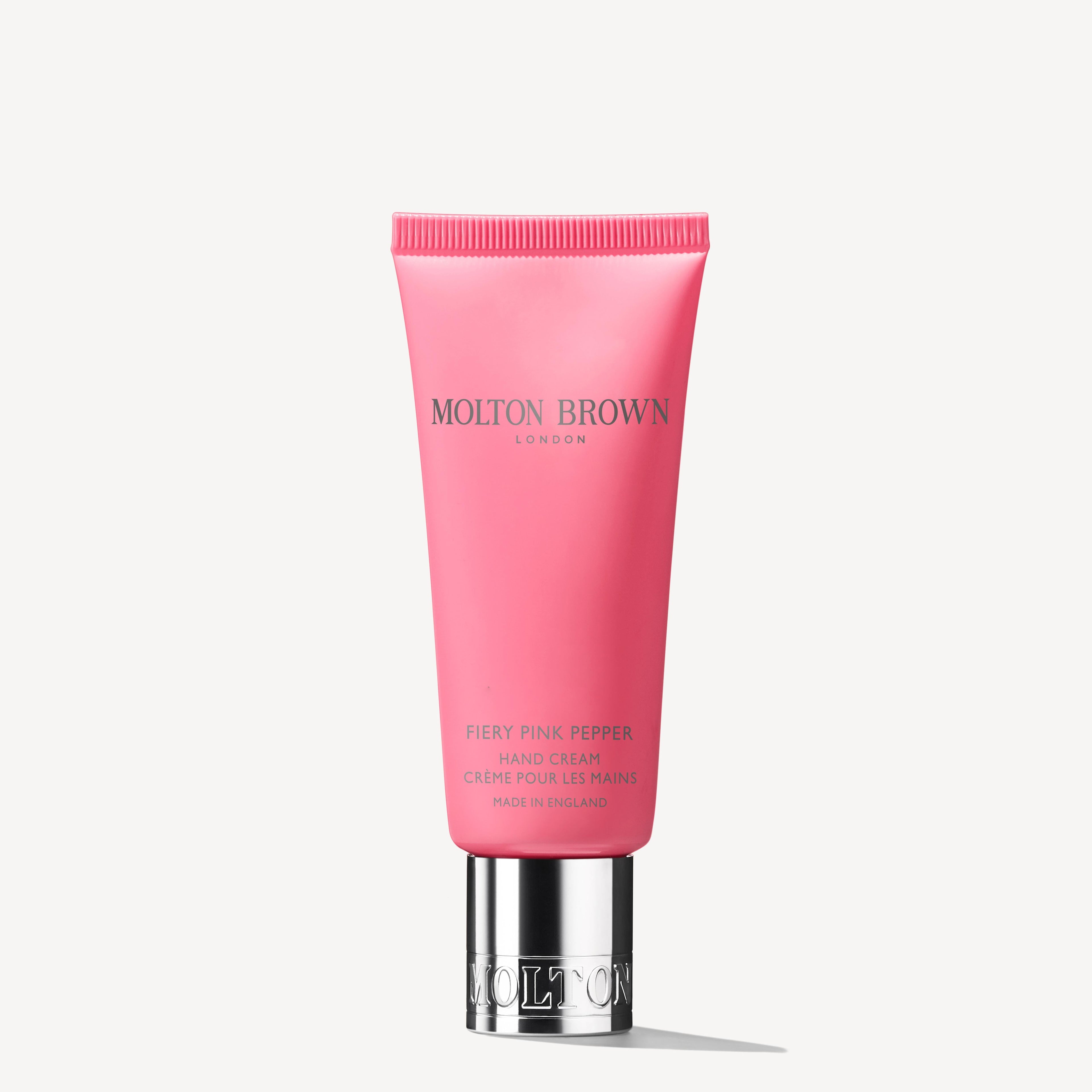 A pink tube of MoltonBrown Nederlands Fiery Pink Pepper Handcrème 40ml with a silver cap, upright on a white background. The text is printed in silver and gold, and the handcrème is enriched with sheaboter.