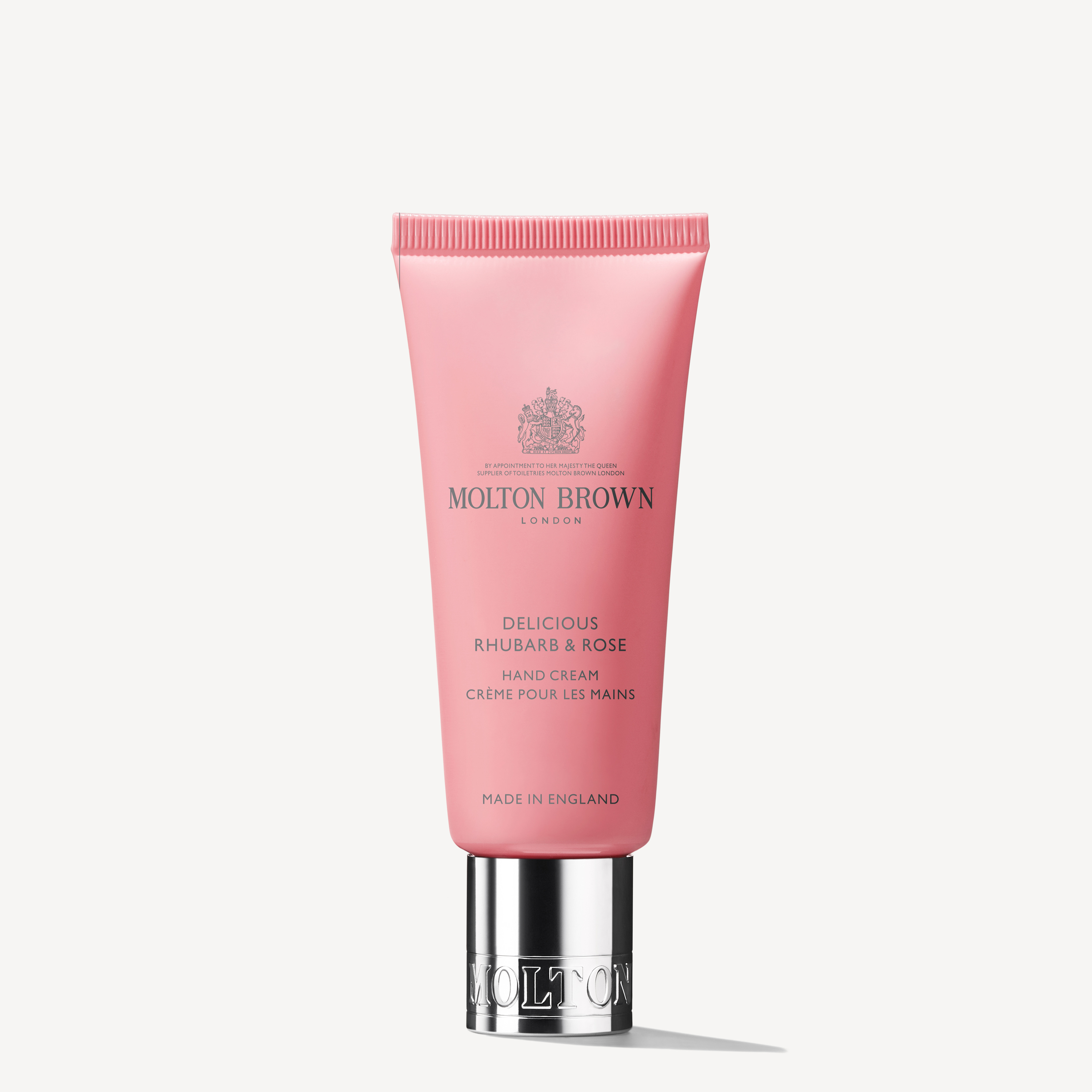 A pink tube of MoltonBrown Nederlands Delicious Rhubarb & Rose Handcrème 40ml with silver cap stands upright on a white background, featuring elegant product details and logo—perfect for droge handen.